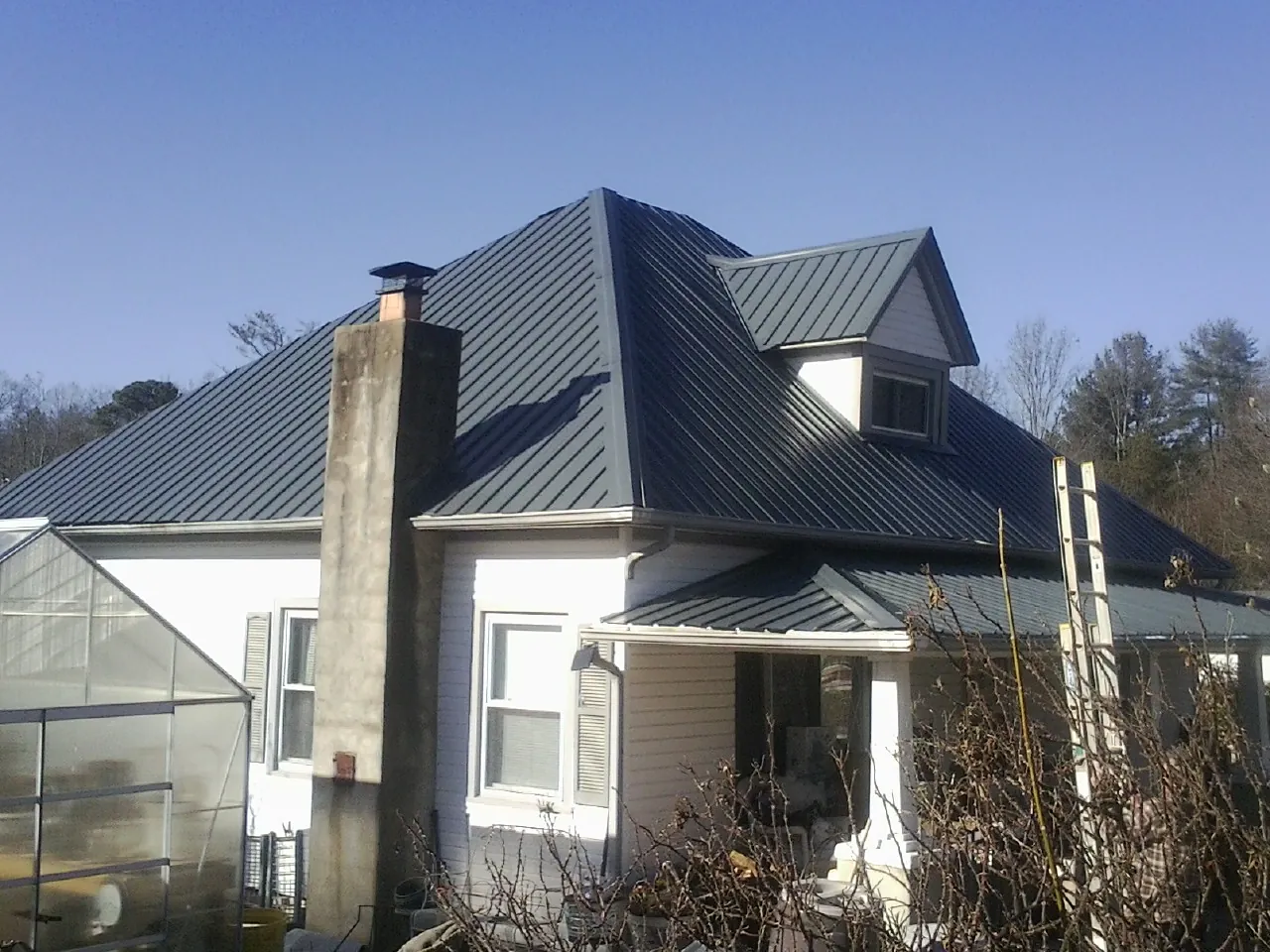 Dark blue standing seam metal roof on a white farmhouse with dormer — Slate & Tile Roof Repair by Roofing Brothers in Mabank