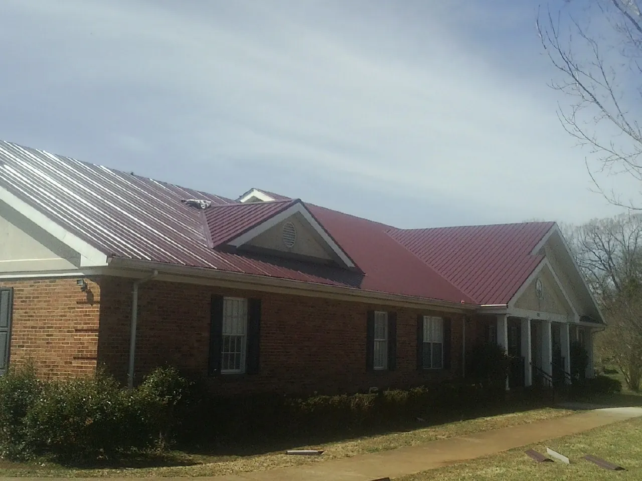 Red metal roof with gabled entries on a long brick building, from a Hail Damage Roof Repair job in Mabank