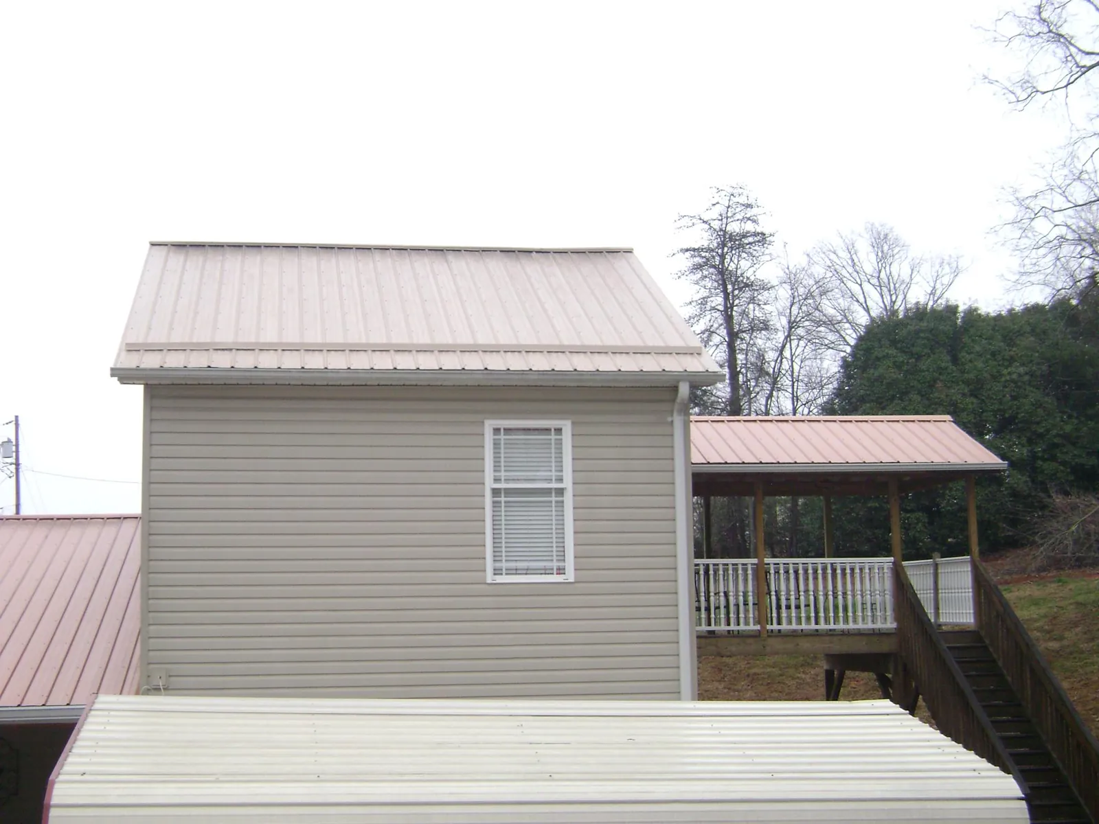 Tan metal roofs on a two story addition and attached porch, from a Roof Replacement job in Mabank